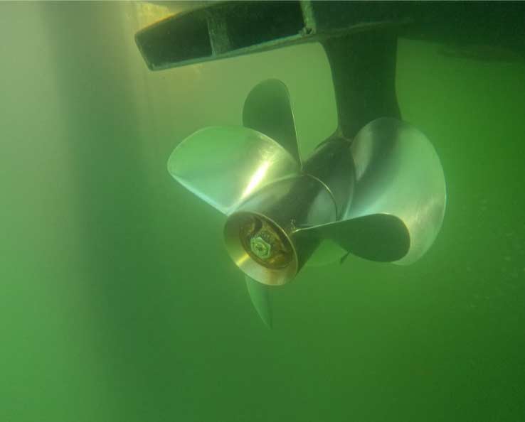 Underwater shot of a three-blade boat propeller in green-tinted water, demonstrating the high-quality results of a professional hull cleaning and inspection service.